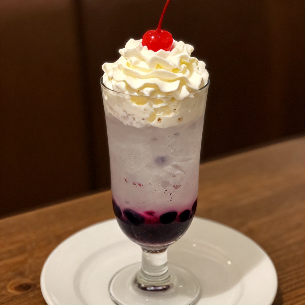 Glass of Italian cream soda with blueberry syrup, whipped cream, and a cherry, on a white plate, warm side lighting